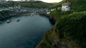 Drone rises from behind cliffs with the village Port Isaac in Cornwall behind.