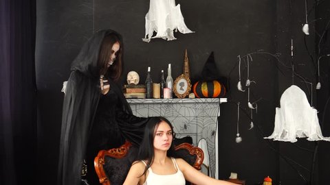Woman in spooky Halloween Death Ripper costume stroking young brunette head in chair in spider web decorated room