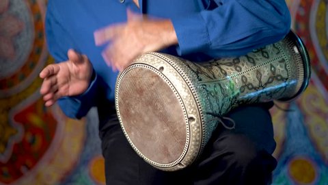 Closeup of hands playing fast rhythm on doumbek drumming slow rhythm with arabic background.