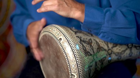 Closeup of hands playing roll on doumbek drumming slow rhythm with arabic background.