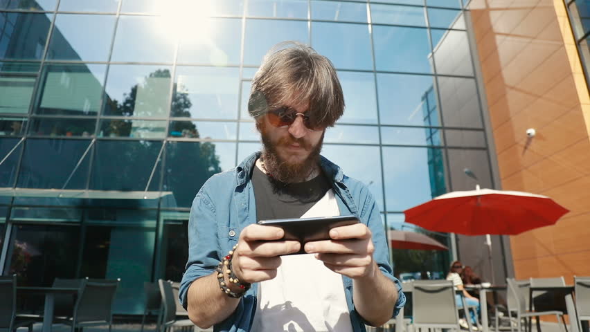 Excited young man playing a game on phone, spending time off with gadget outdoors on typical working day