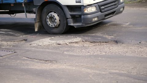 close-up, very poor road coverage, many pits, curved asphalt, a large truck slowly passes a stretch of road in disrepair. the road needs repair.