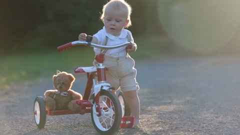 Cute toddler child, boy, playing with tricycle in backyard, kid riding bike on sunset
