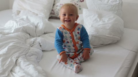 Cute baby boy, smiling and sitting at home in sunny bedroom
