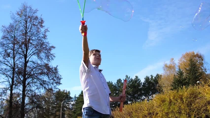 A young guy in the park makes big soap bubbles. Holiday and outdoor entertainment