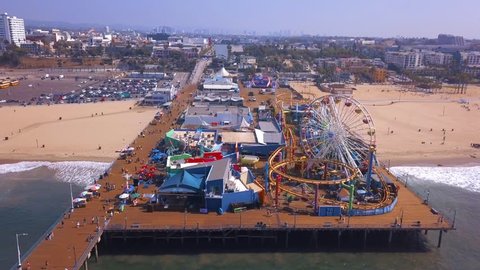 Early morning aerial view of the Santa Monica pier during a sunny day with amusement park view and people walking around in Los Angeles.