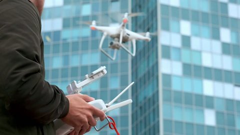 Young man flying quadro drone with modern white RC transmitter. Male filmer controlling drone over RC radio controller. Man filming with drone camera near industrial city and high-tech building