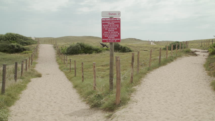 A sandy path splits into two. A man picks a path to walk down.