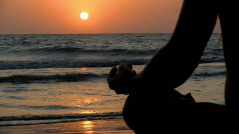 Young man practicing relaxation exercises by the sea. Golden sunset over the sea practicing yoga. Sunset on the beach meditating in front of the sun.
