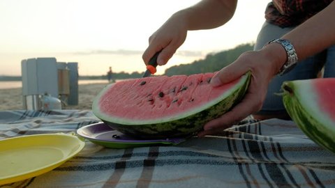 Happy girl eating slices of watermelon on the beach. Father slicing a watermelon Summer picnic outdoors. 4k