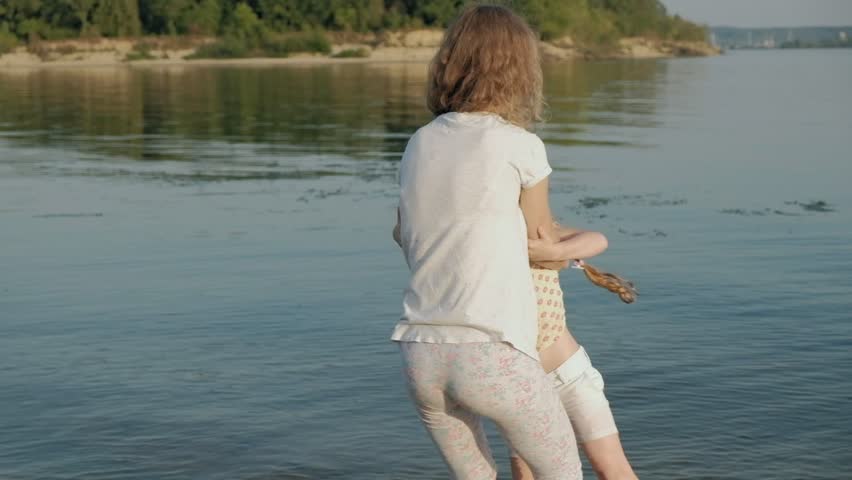 Close-up of mother and daughter playing together. A young mother is spinning his daughter at the beach of the sea shore super slow motion 4k