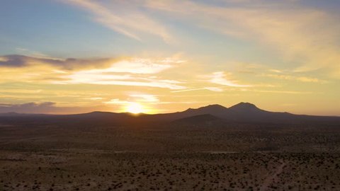 Aerial, flying toward a golden sunrise over a Mojave Desert mountain landscape