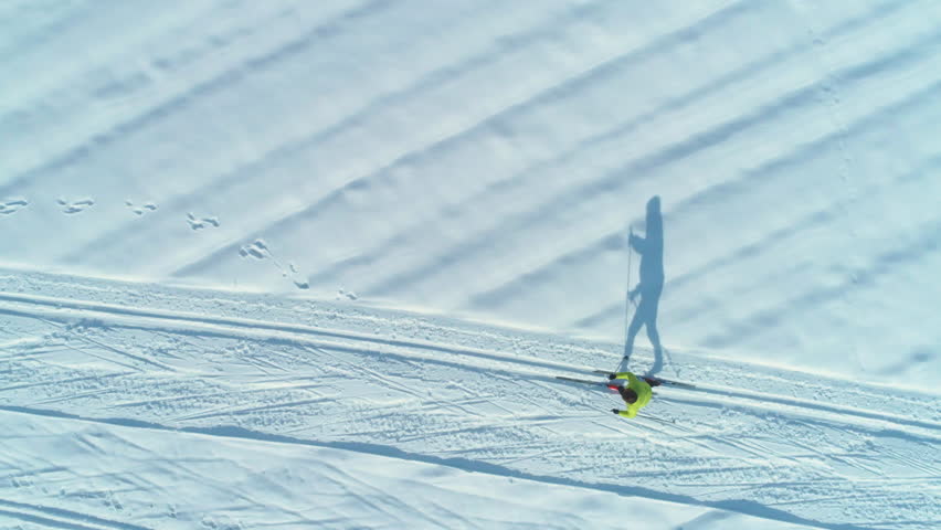 AERIAL, TOP DOWN: Flying above energetic woman skiing down the narrow trails on a sunny day. Cinematic shot of active female tourist cross country skiing during fun winter holiday in scenic Slovenia.