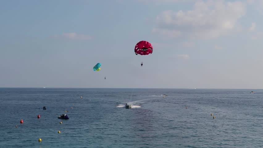 Parasailing in Nice, France, August 2018. Parasailers with red canopy, towed by boat, come nearer camera and land in water.