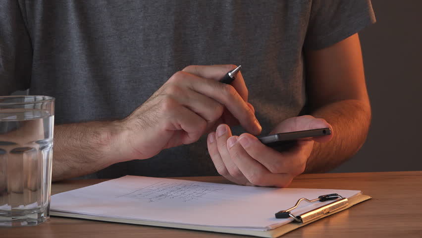Using smartphone and taking notes, close up of male hands writing in notepad while simultaneously typing on mobile phone touch screen Royalty-Free Stock Footage #1017362083