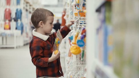 Footage little boy is standing of the shop and choosing toys. 4k video