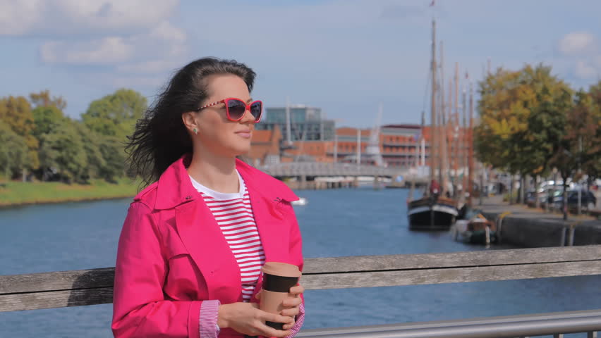 Attractive woman with coffee cup standing at bridge in sunny day and enjoying city view