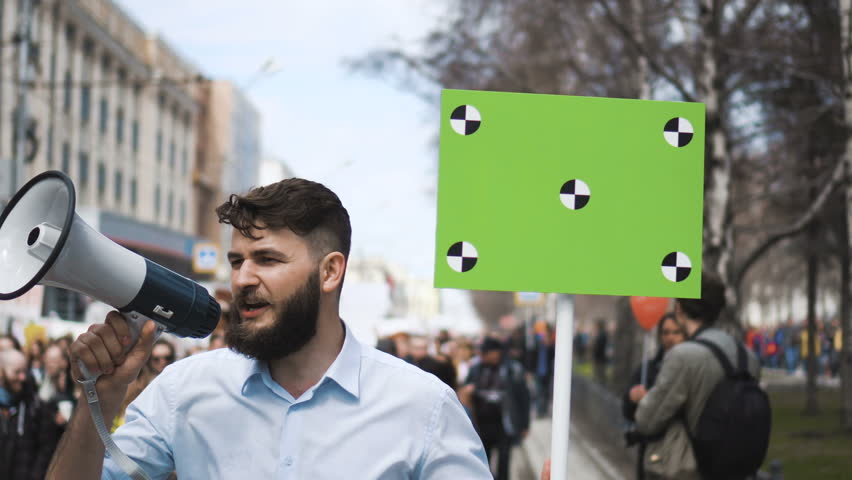 Angry adult young man. Banner hand. Go shout loudspeaker rally. Aggressive protester strike. Revolution city during day. Crowd people in the background on street. Caucasian boy. George Floyd racism. Royalty-Free Stock Footage #1017372403
