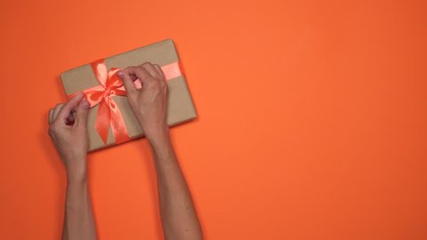 Woman hands placing gift boxes over orange flat lay