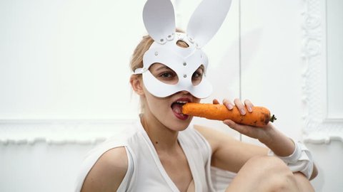 Close up of woman in a mask of hare eating carrots. Halloween party and celebration concept. Concept leather mask BDSM