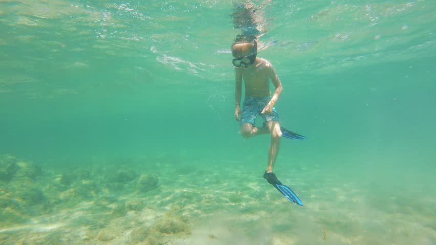 Little boy with flippers, mask and snorkel swimming and diving in the sea, action camera underwater footage