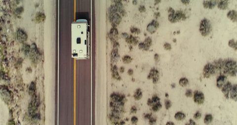 AERIAL - Topdown view of an RV in the desert while the camera tilts up and shows the RV driving towards a landscape