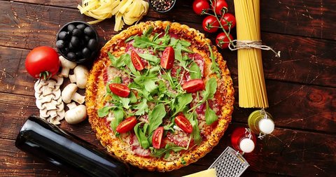 Italian food background with pizza, raw pasta, spices, herbs, wine, and vegetables on wooden table. Top view.