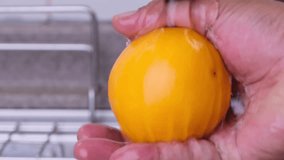 Man's hand rinsing orange fruit with water at the kitchen sink. 