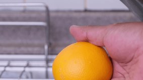 Man's hand rinsing orange fruit with water at the kitchen sink