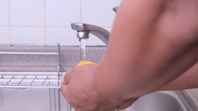 Man's hands rinsing orange fruit in the sink