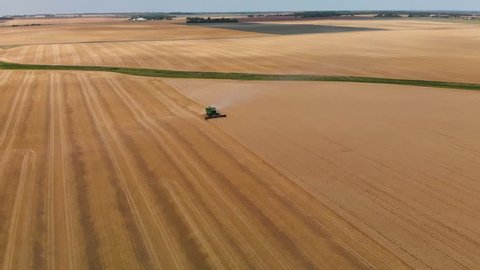 An aerial flyover of a farmer in a combine harvesting a wheat field.