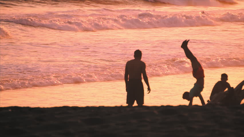 Young man walking on hands on pink sunset beach in Guatemala