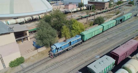 Aerial View. Locomotive with carriages moves along the railway tracks in the industrial area.