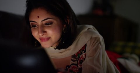 4K Close up panning shot of smiling Indian woman looking at computer screen late at night