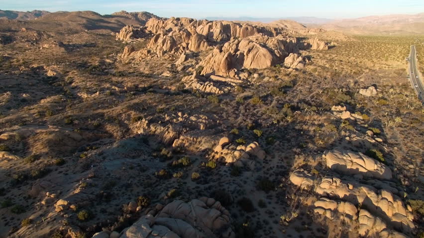 Fast aerial flying towards rock formations in Joshua Tree National park with orange sunset
