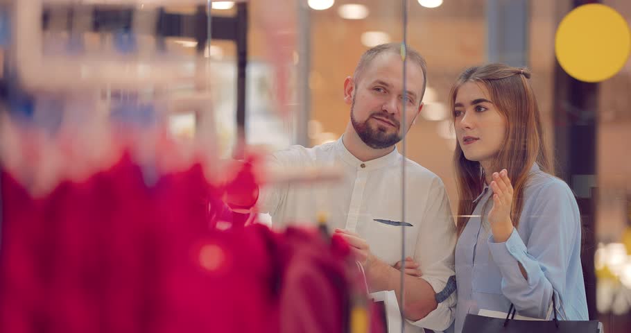 Happy couple in the mall, the girl shows something behind shop window | Shutterstock HD Video #1017417856