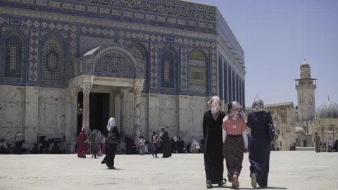 A slow motion shot of people walking around the Dome of the Rock at the Al Aqsa Mosque in Jerusalem, on a hot sunny day.