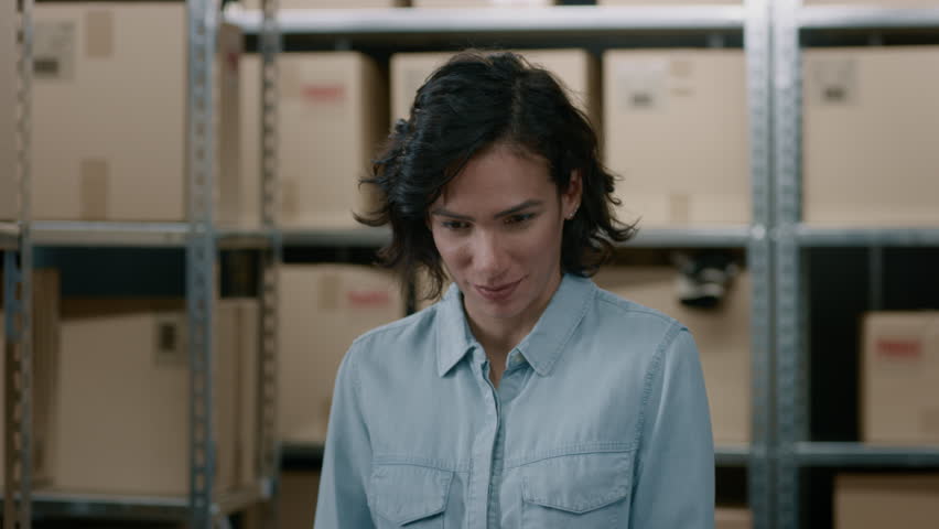 Portrait of the Beautiful Female Warehouse Inventory Manager Standing and Smiling Charmingly. Talented Career Woman Posing with Rows of Shelves Full of Cardboard Boxes and Parcels Ready for Shipment.  | Shutterstock HD Video #1017422845