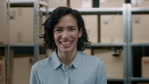 Portrait of the Beautiful Female Warehouse Inventory Manager Standing and Smiling Charmingly. Talented Career Woman Posing with Rows of Shelves Full of Cardboard Boxes and Parcels Ready for Shipment. 