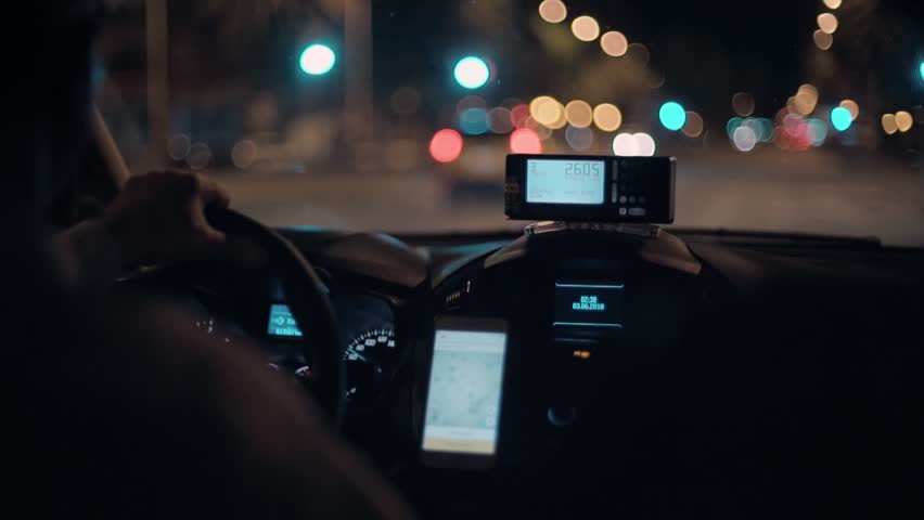 Taxi driver drives cab through night city streets or highway road, uses smartphone for navigation or uses shared economy phone app to find passengers or clients, taximeter counts fare Royalty-Free Stock Footage #1017430237