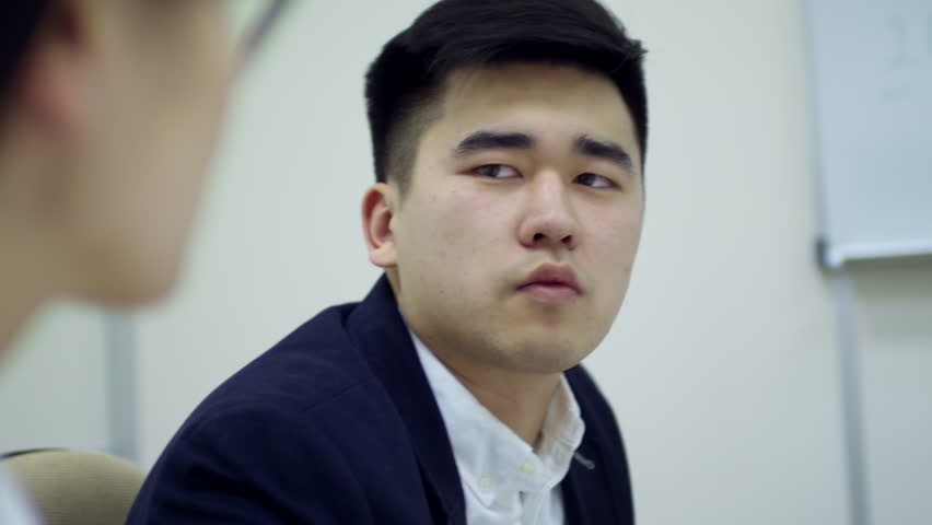 Medium shot of young Asian man sharing thoughts on project when having meeting with business partners or colleagues | Shutterstock HD Video #1017431041