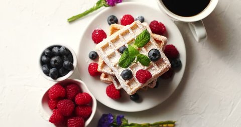 From above shot of cup of aromatic coffee and bowls with fresh berries standing near plate with delicious soft waffles