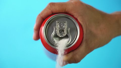 Red soda can pouring out white sugar on a bright blue background showing an example of how bad sugar and how we all eat to much sugar in health food concept. Slow motion 