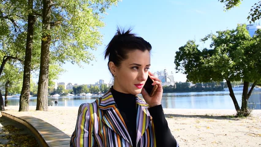 A young woman in a jacket talking on a mobile phone in the city Park
