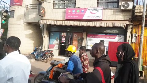 BAMAKO, MALI - CIRCA 2017: View from the humanitarian mission vehicle of the poor street of the Bamako, people commuting on motorcycles waiting at red light in front of Microcred microfinance loans