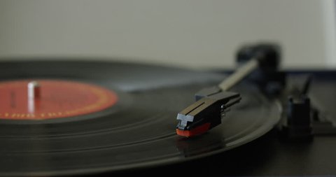 Womans hand takes needle off of playing vinyl record - close up