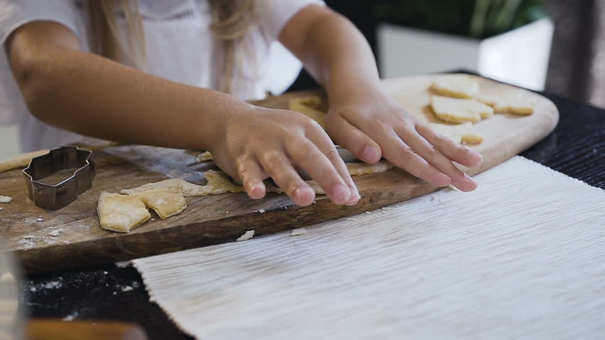 Little girl is baking cookies. Close-up of small girl is rolling out pastry and using cutters. Little girl makes dough for gingerbread cookies at home kitchen, slow motion Royalty-Free Stock Footage #1017464329
