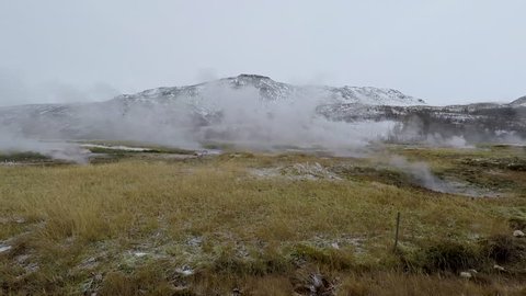 Field of Icelandic geysers smoking on a overcast day with a mountain in the background