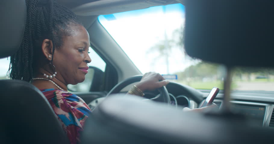 An Uber of Lyft type driver checks the ride sharing app on her smart phone to verify the assignment then engages passenger in friendly conversation. Royalty-Free Stock Footage #1017477580