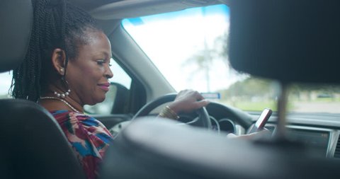 An Uber of Lyft type driver checks the ride sharing app on her smart phone to verify the assignment then engages passenger in friendly conversation.
